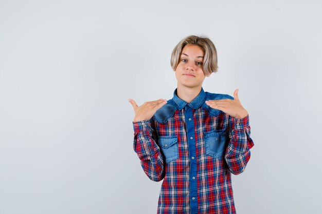 Ragazzo teenager che mostra gesto di altezza in camicia a scacchi e sembra gioioso. vista frontale.