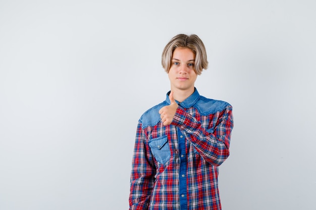 Ragazzo teenager che mostra pollice in su in camicia a scacchi e sembra soddisfatto, vista frontale.