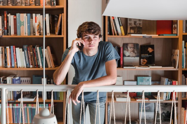 Ragazzo teenager che parla sullo smartphone in biblioteca