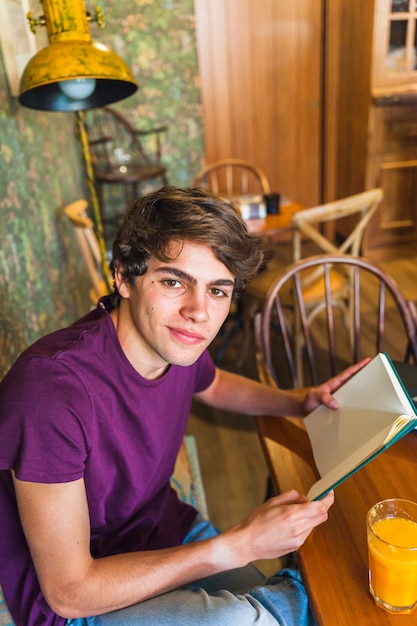 Ragazzo teenager con il libro che guarda l&#39;obbiettivo nel caffè