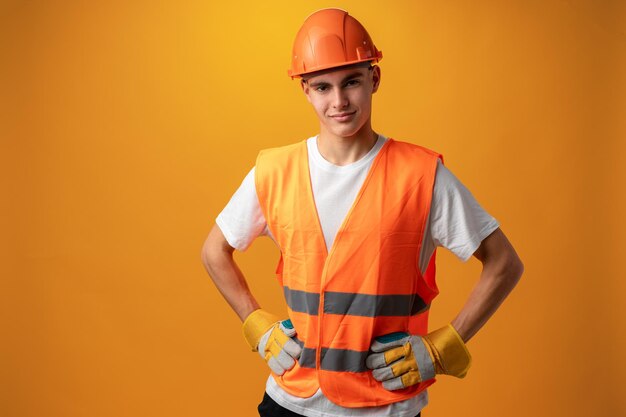 Ragazzo teenager sorridente sicuro che porta cappello duro arancione su sfondo giallo