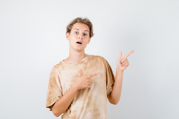 Ragazzo teenager sveglio che indica all'angolo in alto a destra in t-shirt e sembra perplesso. vista frontale.