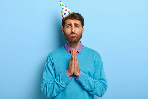 Ragazzo triste con cappello di compleanno in posa in maglione blu