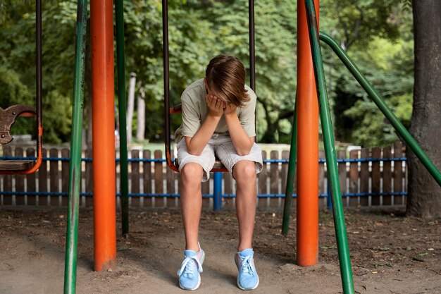 Ragazzo triste del colpo pieno che si siede sull'oscillazione