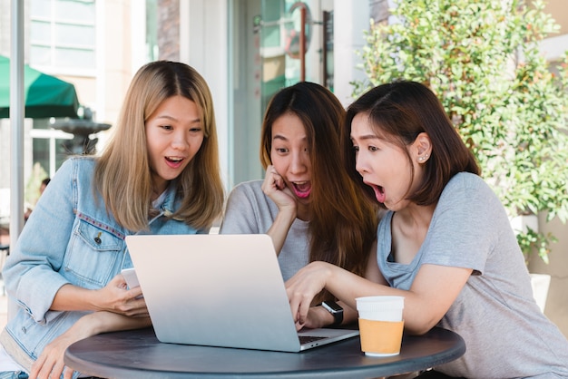 Raggruppi gli amici asiatici felici delle donne che guardano il contenuto di media in linea in computer portatile che si siede nella caffetteria