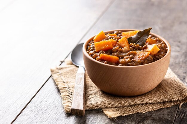 Ragù di stufato di lenticchie con zucca e carote in una ciotola sul tavolo di legno