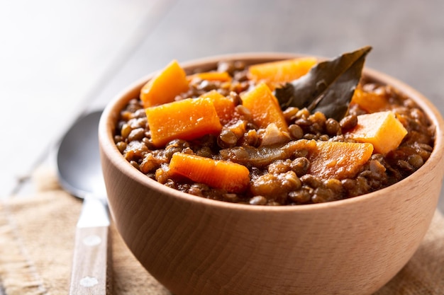 Ragù di stufato di lenticchie con zucca e carote in una ciotola sul tavolo di legno