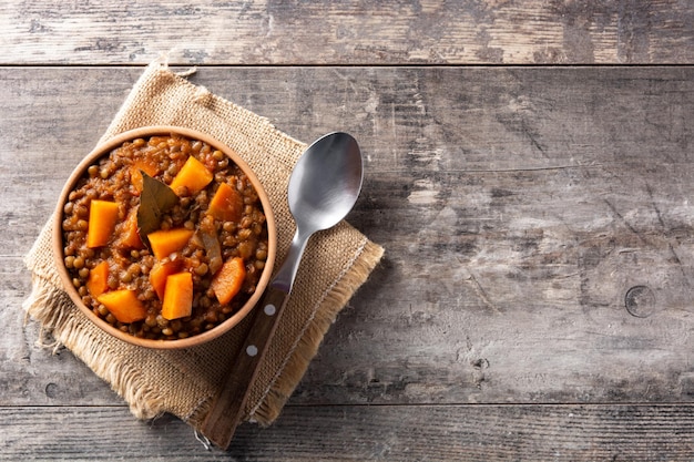 Ragù di stufato di lenticchie con zucca e carote in una ciotola sul tavolo di legno