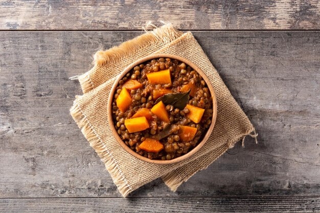 Ragù di stufato di lenticchie con zucca e carote in una ciotola sul tavolo di legno