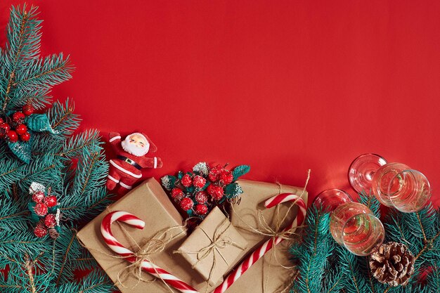 Ramo di abete, confezione regalo e due bicchieri di champagne su sfondo rosso