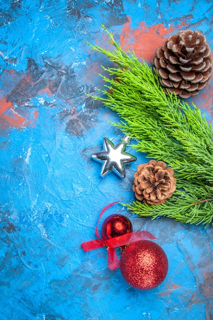 Ramo di pino vista dall'alto con pigne e giocattoli colorati dell'albero di natale su superficie blu-rossa