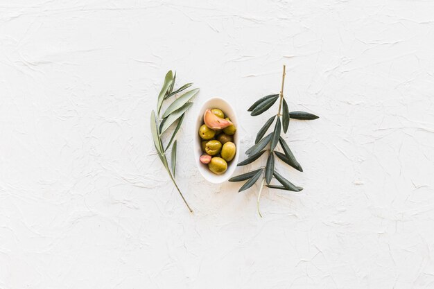 Ramoscelli con la ciotola di olive e spicchio d&#39;aglio su fondo strutturato