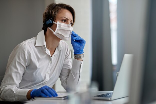 Rappresentante del servizio clienti che indossa una maschera protettiva mentre lavora al call center durante l'epidemia di virus