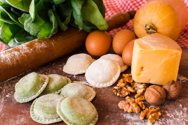 Ravioli crudi bianchi e verdi con ingredienti in tavola di legno