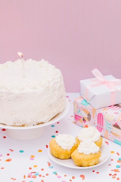 Regali avvolti; cupcake e torta con candela per il compleanno su sfondo rosa