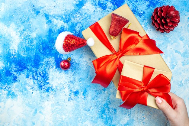 Regali di festa vista dall'alto in mano femminile piccolo cappello di Babbo Natale su spazio libero tavolo bianco blu