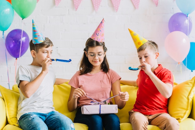 Regalo di compleanno scartare della ragazza mentre i suoi amici che saltano il corno del partito