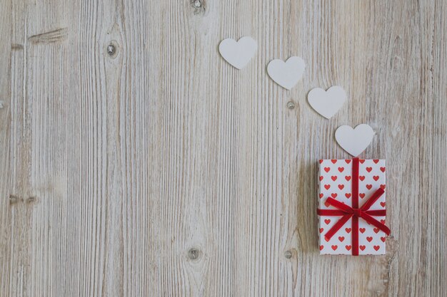 Regalo di pois con fiocco rosso con cuori di carta su un tavolo di legno