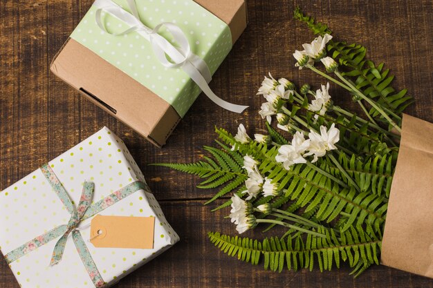 Regalo in scatola con fiori e foglie in sacchetto di carta sul tavolo di legno