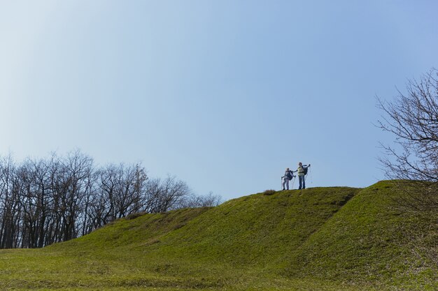 Respirazione piena e libera. Coppia di famiglia invecchiato dell'uomo e della donna in abito turistico che cammina al prato verde vicino agli alberi in una giornata di sole. Concetto di turismo, stile di vita sano, relax e solidarietà.