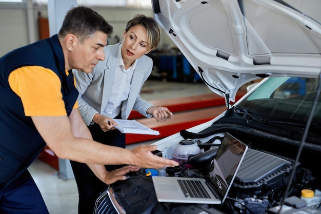 Responsabile femminile e meccanico automobilistico che collaborano durante l'utilizzo del laptop e testano le prestazioni del motore nell'officina di riparazioni auto