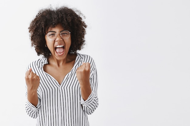 Responsabile ufficio femminile afroamericano infastidito infastidito in camicetta a righe e occhiali stringendo i pugni con emozioni arrabbiate che urlavano e mostravano di essere malati e stanchi di uno stupido collega