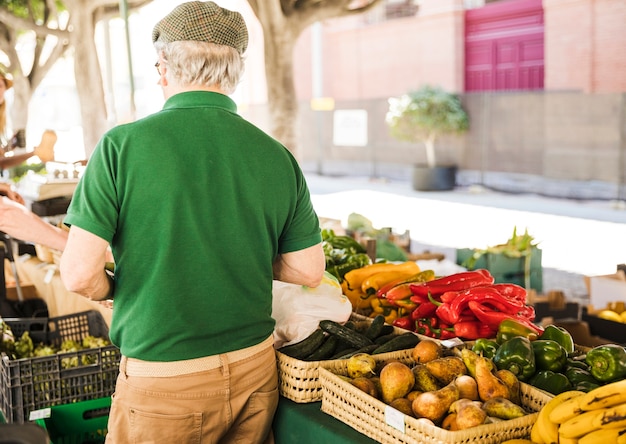 Retrovisione dell'uomo senior che sta alla stalla della frutta e della verdura