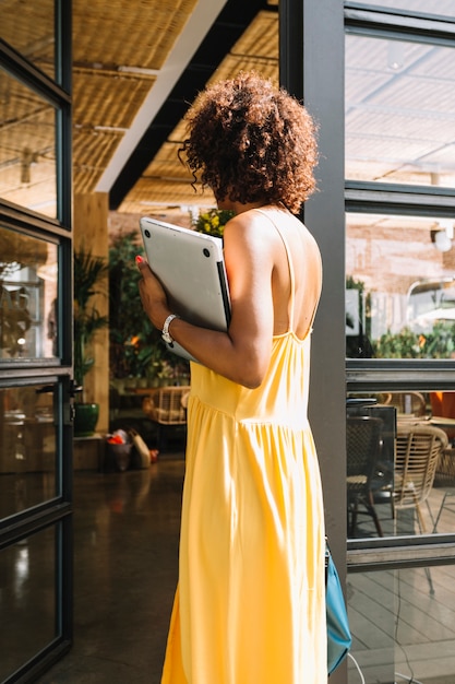 Retrovisione della donna con il computer portatile della tenuta dei capelli ricci