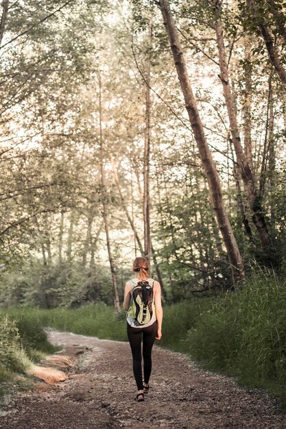 Retrovisione della donna con il suo zaino che cammina sulla traccia della foresta