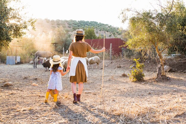 Retrovisione della donna con sua figlia che guarda gli animali nel campo