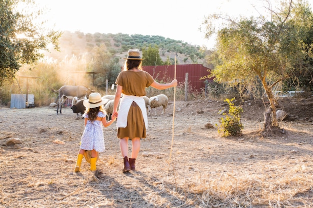 Retrovisione della donna con sua figlia che guarda gli animali nel campo