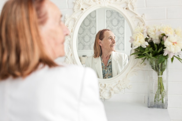Retrovisione della donna senior che si siede davanti allo specchio che osserva via