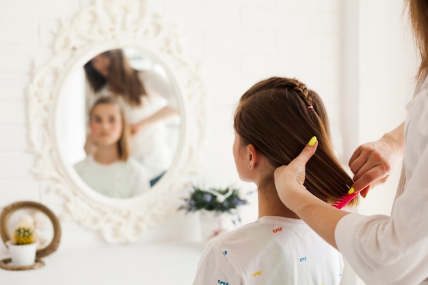 Retrovisione della madre che lega i capelli di sua figlia a casa