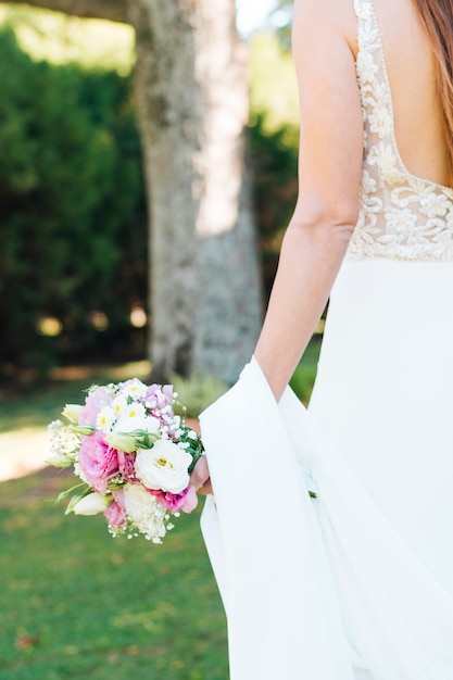 Retrovisione della mano della sposa che tiene il bello mazzo del fiore