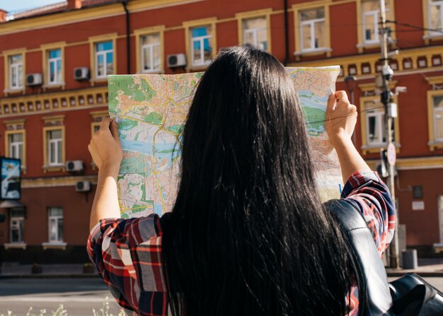 Retrovisione della mappa della lettura della donna con fondo di esterno rosso della costruzione