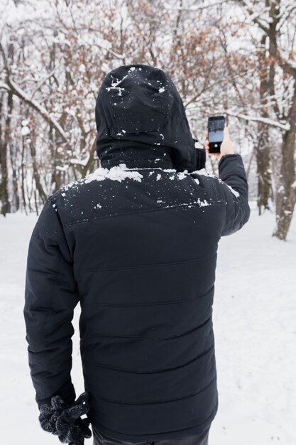 Retrovisione di una persona che cattura maschera tramite il cellulare durante la stagione invernale