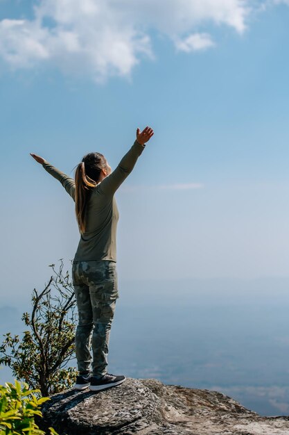 Retrovisione posteriore della giovane donna asiatica che si leva in piedi e si alza con le mani felici sul sentiero nello spazio della copia della foresta della natura