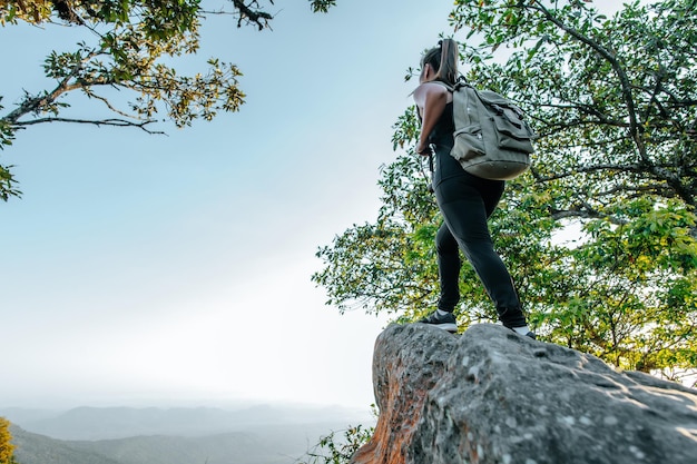 Retrovisione posteriore della giovane donna asiatica che si trova in piedi al punto di vista e che sembra bella vista con felice sulla montagna di picco e sullo spazio della copia del raggio di sole