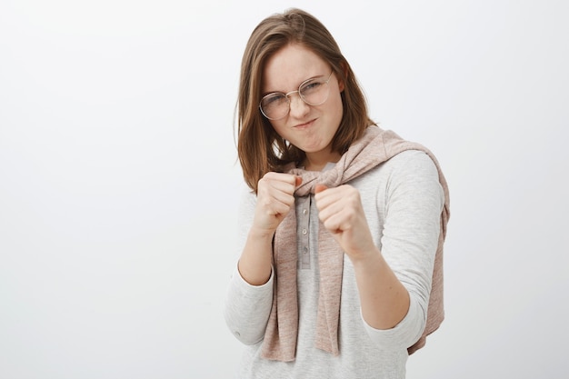 ribelle audace e giocosa amica con gli occhiali e la felpa legata sul collo alzando i pugni serrati e facendo smorfie facendo un'espressione divertente e pericolosa come se combattesse