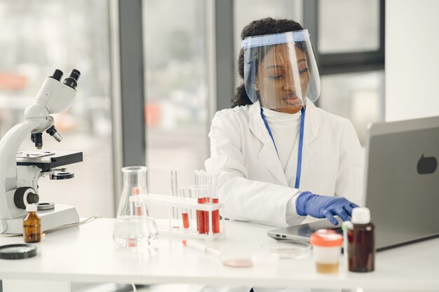 Ricerca di laboratorio sul sangue, concetto di coronavirus. Donna africana che ispeziona il sangue e usa il laptop.