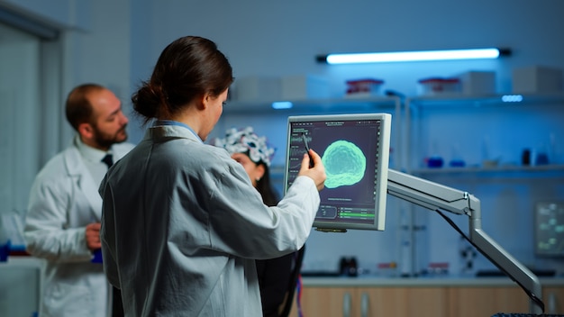 Ricercatore che guarda il monitor analizzando la scansione cerebrale mentre il collega discute con il paziente in background su effetti collaterali, funzioni mentali, sistema nervoso, scansione tomografia che lavora in laboratorio