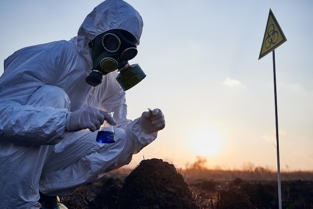 Ricercatore in tuta protettiva che lavora su un campo bruciato prelevando campioni di flora