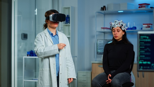 Ricercatore professionista che indossa occhiali per realtà virtuale utilizzando innovazioni mediche in laboratorio che analizzano la scansione cerebrale del paziente. Team di medici neurologici che lavorano con dispositivi di simulazione ad alta tecnologia dell'attrezzatura