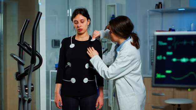 Ricercatore scienziato che prepara una paziente donna per il test di resistenza che attacca gli elettrodi su apparecchiature per il corpo professionale. Team di medici che monitorano lo stato di salute di patinet, vo2, la scansione ekg viene eseguita sullo schermo del computer