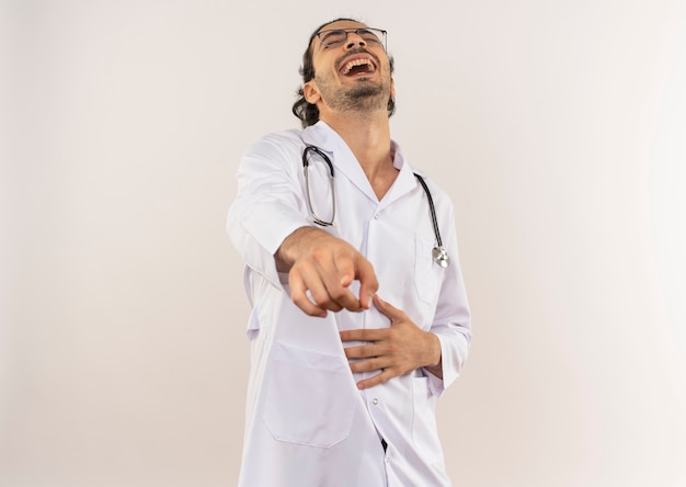 Ridendo giovane medico maschio con occhiali ottici che indossa una veste bianca con uno stetoscopio che ti mostra il gesto