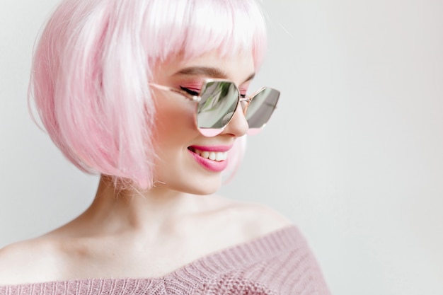 ridendo sognante giovane donna indossa occhiali da sole scintillanti e peruke. Ritratto del primo piano dell'interno della ragazza estatica sorridente con i capelli rosa.