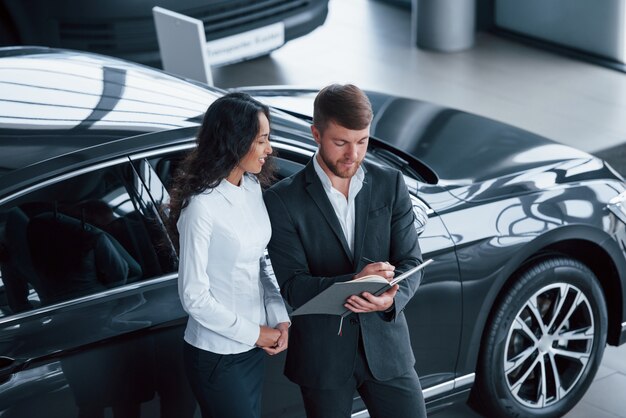 Riempire i documenti. Cliente femminile e uomo d'affari barbuto elegante moderno nel salone dell'automobile