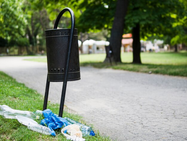 Rifiuti di plastica su erba vicino al bidone della spazzatura al parco