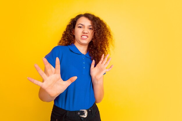 Rifiuto, disgustato. Ritratto della ragazza dell'adolescente caucasico sul fondo giallo dello studio. Bello modello riccio femminile in camicia. Concetto di emozioni umane, espressione facciale, vendite, pubblicità, educazione. Copyspace.