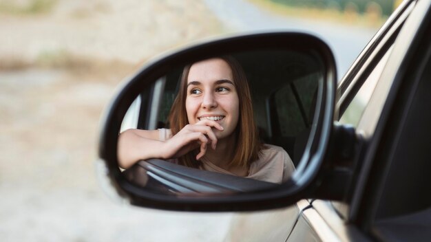 Riflessione della donna di smiley nello specchio dell'auto